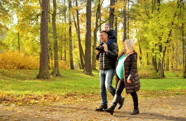 Fototapeta premium Pregnant young woman walking in autumn park with her husband and child