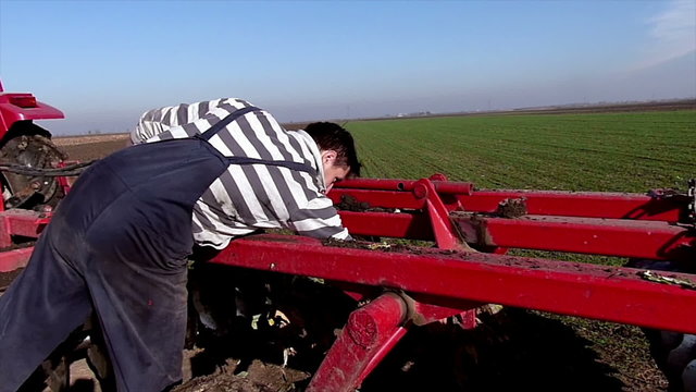 Young farmer cleaning the land cultivating machine on field. Slow motion video. High speed camera.