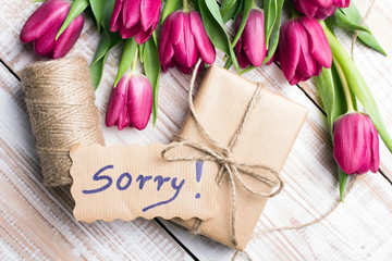 word SORRY and bouquet of tulips on wooden background