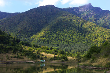 Fototapeta na wymiar Small house near water in high mountains background