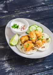 Crispy fried fish on a homemade tortilla on a dark wooden background