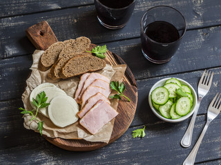 Delicious appetizer to wine. Smoked ham, cheese and two glasses with red wine on dark wooden background