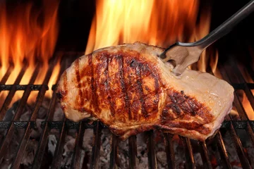 Gardinen Schweinelendesteak auf heißem flammendem Barbecue-Grill mit Gabel © Alex