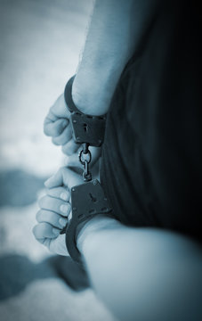A man hands in handcuffs behind his back. Selective focus with shallow depth of field.