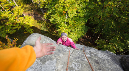 Young beautiful woman climbing in the nature on large boulder, her male partner giving her a hand....