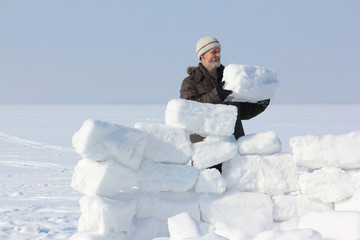 The man with a beard in a gray cap building an igloo of snow blo