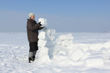 The man with a beard in a gray cap building an igloo of snow blo