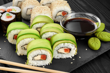 Sushi rolls with avocado, salmon and sesame seeds on slate tray.
