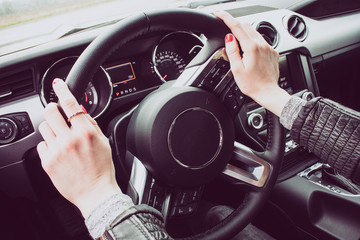 Close up image of female driver hands on the steering wheel. Red painted nails.