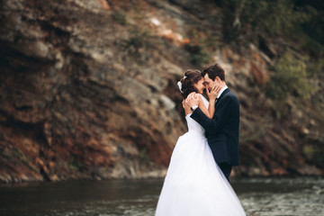 Obraz premium Elegant gentle stylish groom and bride near river with stones. Wedding couple in love
