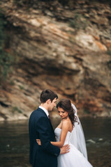 Fototapeta premium Elegant gentle stylish groom and bride near river with stones. Wedding couple in love