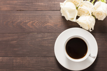 A cup of coffee with white roses on wooden background