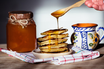 Russian Maslenitsa: Pancakes on a wooden plate, painted ceramic milk jug and fresh honey