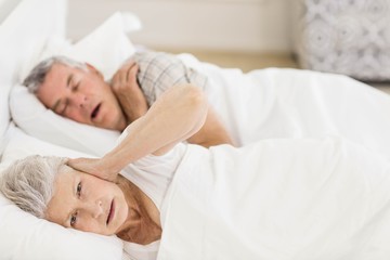 Obraz na płótnie Canvas Awake senior woman in bed covering her ears