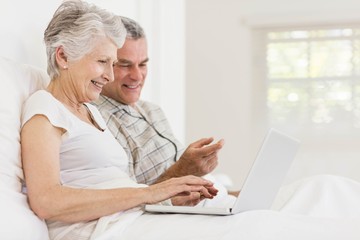 Senior couple using laptop at bed