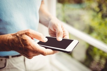 Senior man next to the window using smartphone