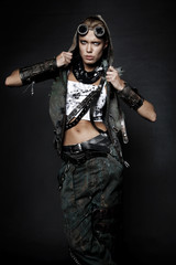 Young woman in brutal style clothes with goggles on studio black background