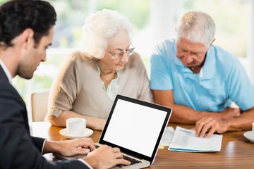 Businessman using laptop while senior couple is reading document