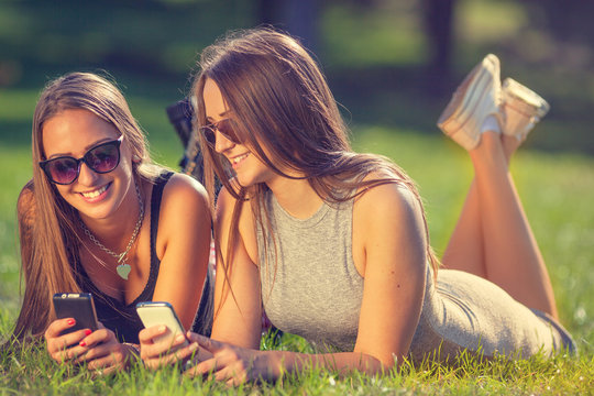 Two young girls smiling and using your smartphones