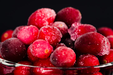 frozen cranberries in a glass bowl on black background