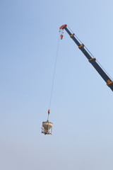 Crane lifting concrete mixer container against sky
