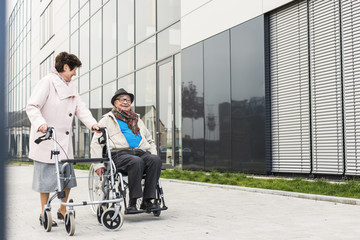 Senior woman with wheeled walker and senior man in wheelchair on pavement