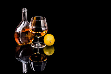 Bottle with Goblet of Brandy and lemon on the mirror black surfa