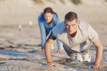 Fototapeta premium Young couple doing push ups on ocean beach