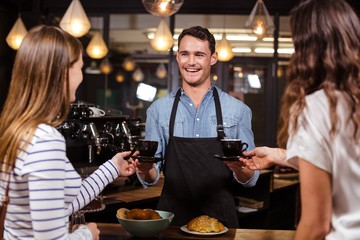 Smiling barista giving coffees to women