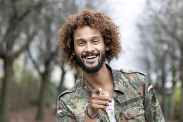 Portrait of smiling man with dyed ringlets wearing camouflage shirt pointing on viewer