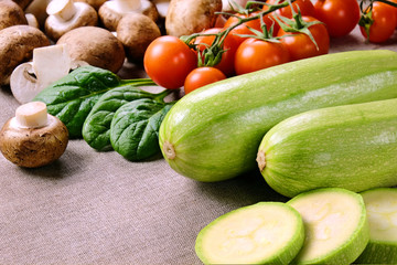 Two whole and one chopped zucchini slices, cherry tomatoes, mushrooms and spinach leaves on a linen fabric.