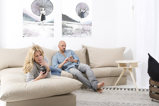 Mature couple sitting on sofa using their smart phones