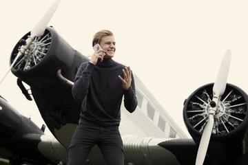 Young man on cell phone in front of vintage propeller plane