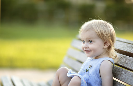 Portrait of smiling blond little girl sitting on park bench