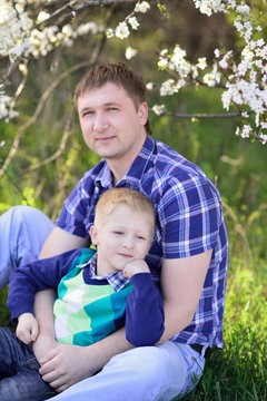 Dad and son sitting on green spring grass on a background of a b