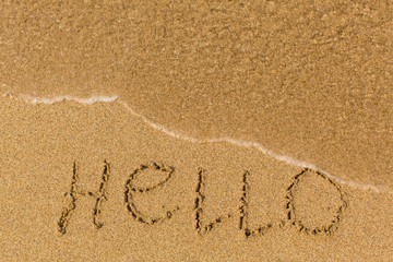 Hello - word drawn on the sand beach with the soft wave.