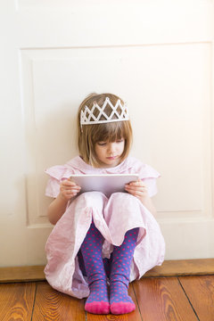 Little girl dressed up as a princess looking at digital tablet