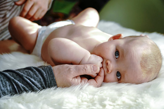 Grandmother's hand touching baby girl lying on a white fur