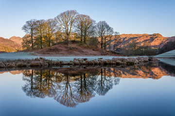 Frosty winter morning at River Brathay In Elterwater, Lake District, UK. Clear reflections of trees...