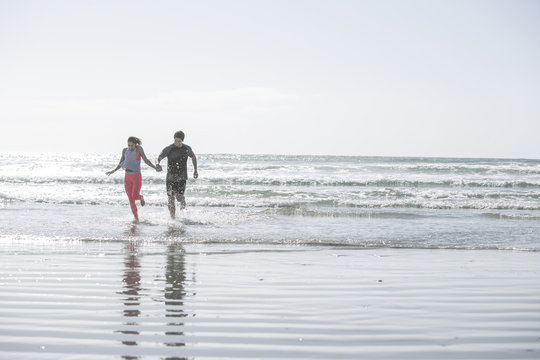 Young man and woman running hand in hand in the ocean