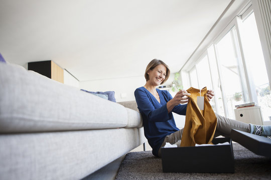 Smiling woman at home unpacking parcel with garment