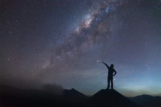 Woman is standing on the hill and pointing the Milky Way.