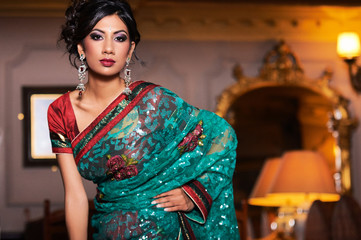 Obraz na płótnie Canvas Unique portrait of oriental indian indoor model dressed with colorful saree and wearing asian jewellery and strong makeup