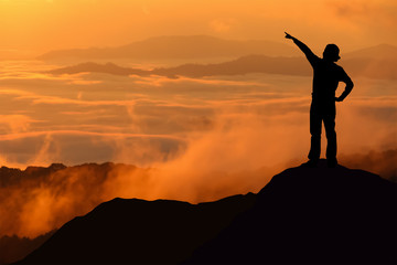 Silhouette of tourist woman standing and pointing on top of a mountain.