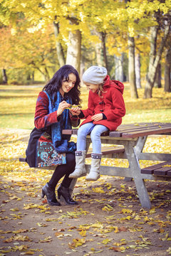 Mother with daughter in autumnal park examining leaf