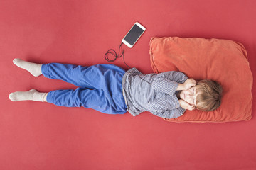 Little boy lying on bed hearing music with smartphone and earphones