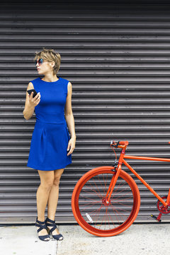 Woman with smartphone and red racing cycle waiting in font of roller shutter