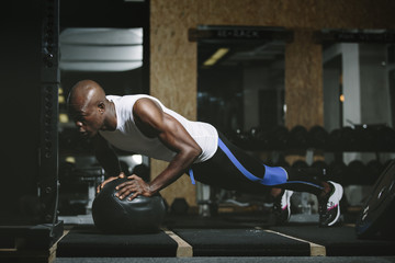 Physical athlete doing push-ups on medicine ball in gym