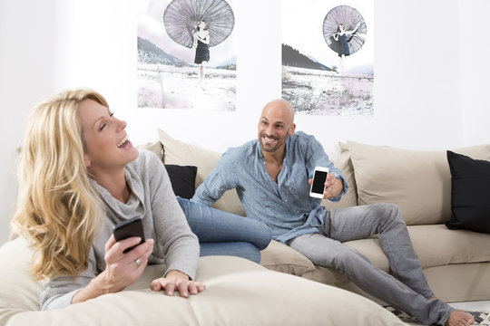 Mature couple sitting on sofa using their smart phones