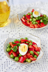Colorful salad with green peas, red pepper and quail egg in a bowl, closeup